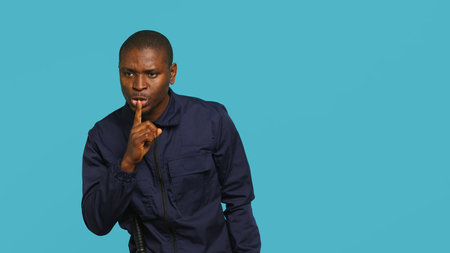 Security guard doing shush sign gesturing with finger, preventing public access in restricted area. Portrait of stern bodyguard urging people to keep quiet, studio background, camera Aの写真素材