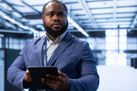 Technician in data center using device to identify and solve technical issues related to data center infrastructure. IT specialist managing, maintaining and securing server hub environmentの写真素材