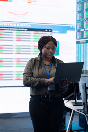 Chief financial officer studying capital funds and revenue data on big screen and laptop, verifying...