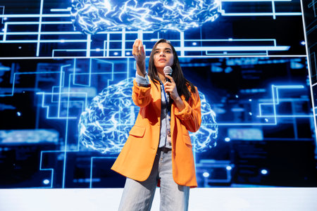 Speaker holding motivational speech at event bringing together industry experts to share insights on latest advancements in AI tech. Indian woman speaking at business expo in front of entrepreneursの写真素材