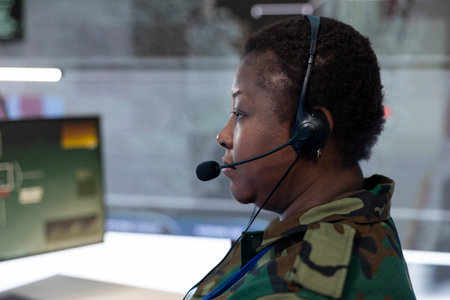 Female IT operator examining real time battlefield data on big screen, collecting intelligence for a reconnaissance defense operation. Military staff provides support for an infantry unit. Close up.の写真素材