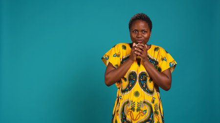 Woman in traditional ethnic clothing drinks a sip from coffee cup, serving a fresh caffeine beverage with amazing roasted aroma. Happy pleased girl drinking a refreshment in studio. Camera B.の写真素材