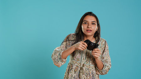 Focused woman playing videogames with motion controlled joystick, studio background. Gamer participating in online multiplayer racing game using gyroscope function on gamepad, camera Aの写真素材