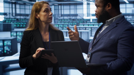 Teamworking colleagues in server farm using laptop to patch network issues affecting transfer rates. Coworkers in data center doing brainstorming, fixing errors affecting supercomputers, camera Aの写真素材
