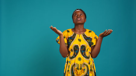 Wishful young adult with belief in religion praying in studio, hoping for good things against blue background. Hopeful spiritual girl. Camera B.の写真素材