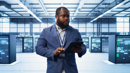 IT technician walking in data center, overseeing server operations using tablet. Expert ensuring optimal performance and data integrity in server hub using digital device, camera Bの写真素材
