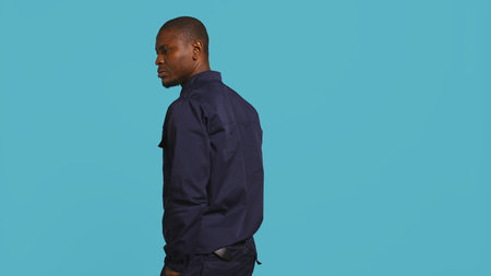 Portrait of security guard overseeing premises to prevent intrusion hearing suspect sounds, turning around. Private law enforcement worker standing isolated with back against studio backdrop, camera Bの写真素材