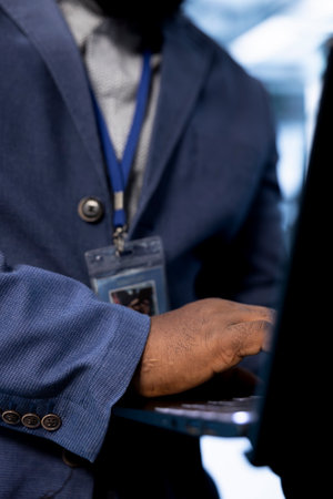 Software developer in data center uses laptop to identify and solve issues related to data center infrastructure. Close up of worker managing, maintaining and securing server farm environmentの写真素材