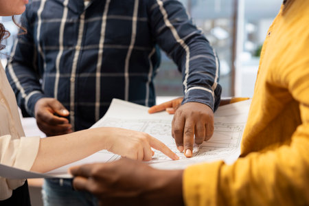 Real estate agents helping clients during an office tour with blueprints, evaluating architectural plans and discussing rental agreement deals. Owner planning corporate relocation. Close up.の写真素材