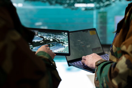 Troopers comparing gathered radar information on laptop and tablet, communicating with allied forces and transmitting real time data from surveillance satellite footage. Joint operations.の写真素材