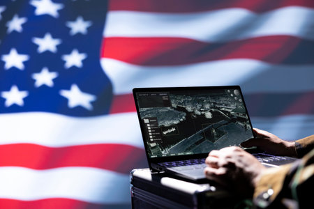 US Air Force officer isolated over USA flag monitoring zone of interest using radar. Close up shot of United States military soldier engaged in surveillance mission using laptop, looking at world mapの写真素材