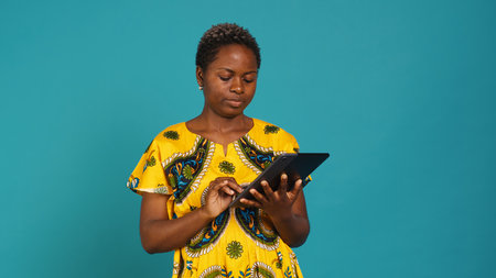 Happy positive adult navigating on online webpages in studio, using portable gadget to browse things on internet connection. Woman in traditional ethnic attire poses against background. Camera A.の写真素材