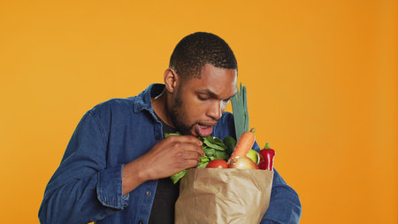 Person counting all his freshly harvested produce in a paper bag, making sure he bought important ingredients for his vegan meals. Male model eating only ethically sourced food. Camera A.の写真素材