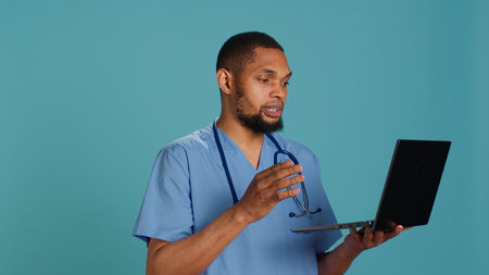 Friendly upbeat medic doctor in videocall meeting using laptop, providing treatment plan. Jolly hospital staff member listening to patient health problems in online telemedicine call, camera Aの写真素材