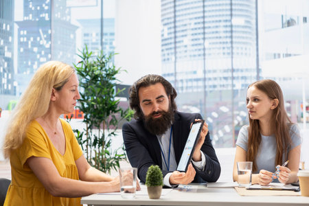 Financial advisor creating reports on investment performance and activity on tablet, showing them to clients. Agent using device to develop portfolio for customers, maximizing financial gainsの写真素材