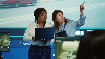Diverse employees monitor and manage urban traffic in control center agency, following cars and...