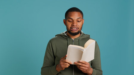 Man reading book aloud, narrating story for audience. Person enjoying literature novel, reciting from pages, entertaining spectators, isolated over studio background, camera Aの写真素材