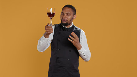 Waiter offering a glass of wine to customers waiting for their food at the table, providing...