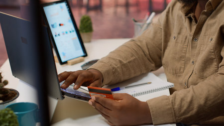 Successful freelancer does online shopping with his credit card, making electronic banking transactions at home office setup. Businessman doing remote work and buying things on laptop. Camera A.の写真素材