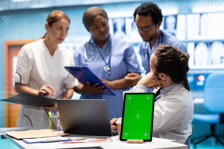 Group of doctors consulting hospital records next to chroma key display, using x ray test results to examine the diagnosis. Diverse experts meeting at private clinic to provide a treatment plan.の写真素材