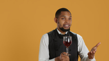 Restaurant employee bringing a glass of red wine to clients at the table, serving people at a five star diner. Waiter with professionalism focusing on customer satisfaction. Camera A.の写真素材