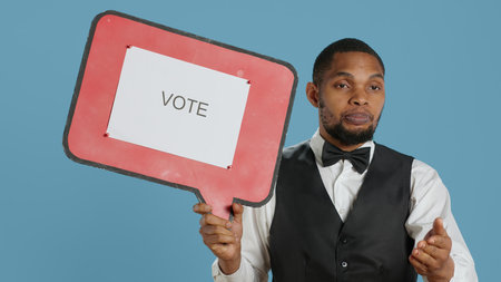 Hospitality industry worker shows speech bubble with message, urging people with cardboard sign advertisement. Hotel porter employee holds icon with commercial ad. Camera A.の写真素材