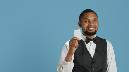 Classy hotel bellboy in tuxedo giving the room access key card to guest after check in, offering excellent concierge services at holiday resort. Employee working in hospitality industry. Camera A.の写真素材