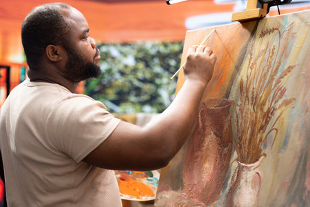 Focused man painting a new rustic artwork on canvas with brushstrokes patterns, mixing watercolors...