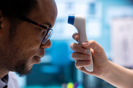 Female doctor taking the temperature of a patient in medical office, checking fever and other flu symptoms at consultation. Physician measuring with a digital thermometer in cabinet.の写真素材