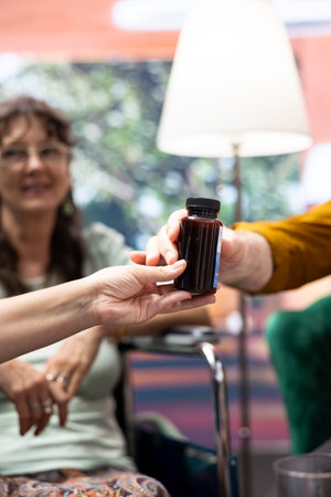 Professional nurse separating pills and medicine in two different bottles, preparing the weekly treatment with daily doses for senior man and woman. Caretaker offer health aid to patients. Close up.の写真素材