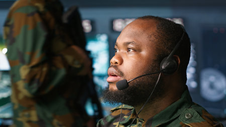 Military dispatcher relays info from army intelligence analysts to troops on front lines, close up shot. Radio communications operator wearing uniform talking in headset mic, camera Aの写真素材