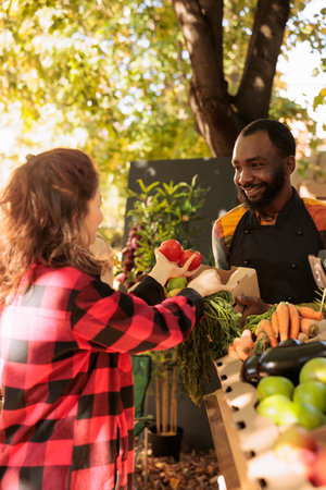 Caucasian woman at a farmers market holding fresh organic produce while talking to african american...