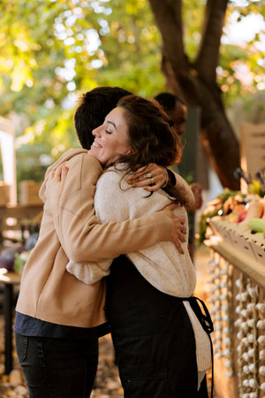 Smiling female individuals hugging each other at eco friendly farmers market, happy vendor enjoys...