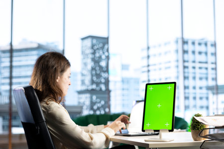 Young business entrepreneur looking at green screen mockup on her gadgets, working in modern urban corporate office. Female leader developing a strategy to increase funding for success.の写真素材