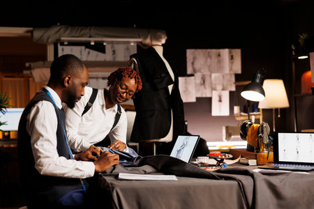 African american suitmakers working with premium quality fabrics in professional tailoring studio. Coworkers making exquisite garments following sketch designs of upcoming sartorial collectionの写真素材