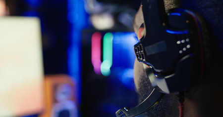 Man playing SF videogame on computer, having fun in neon lit apartment, close up. Gamer competing in online multiplayer game, using headphones to talk with teammates, camera Bの写真素材