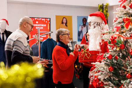 Buyers participate in holiday contest created by employee in santa claus costume, writing names on papers inside box. Senior clients waiting for results to win free clothing items, festive activity.
