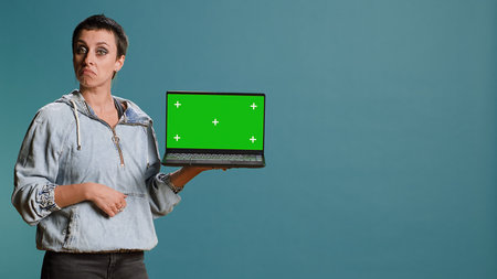 Young adult pointing at laptop with isolated chroma key screen in studio, using modern technology on wireless gadget. Woman with confident style does an advertisement.の写真素材