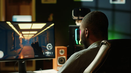 Man in neon lit apartment playing immersive video games on gaming PC at computer desk, handheld camera shot. Gamer competing against enemies in internet multiplayer shooter, camera Aの写真素材