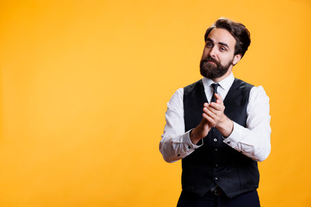 Friendly waiter clapping hands for person, trying to boost confidence and celebrate success in studio. Professional employee at restaurant applauding someone and presenting his congratulations.の写真素材
