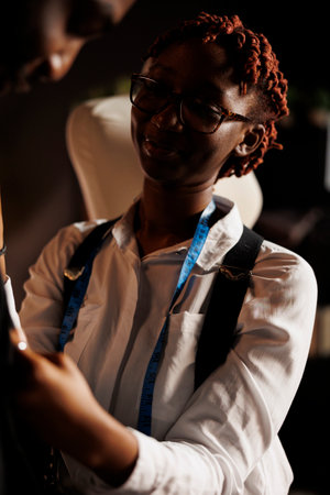 Close up of african american seamstress taking measurements of client for bespoken handmade premium suits. Professional fashion designer helping gentleman pick quality sartorial garmentsの写真素材
