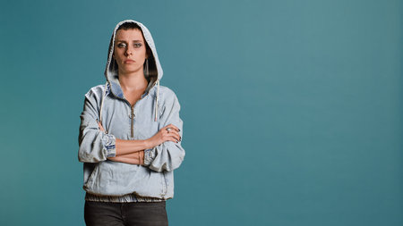 Bold serious woman putting her hood on and acting tough in studio, posing with arms crossed and...