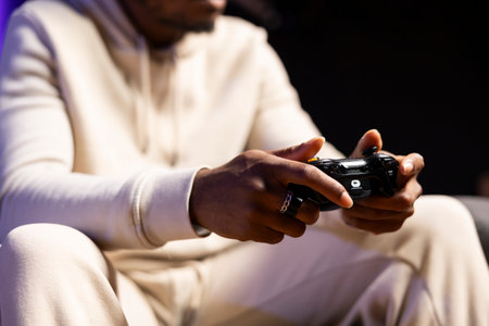 Close up shot of gamepad held by man playing entertaining videogame in rgb lit apartment. Focus on...