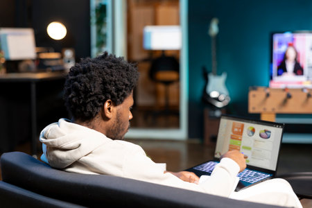 African american self employed man working in personal office, checking statistical data financial graphs on laptop screen. Remote worker in apartment comparing business graphic economic figuresの写真素材