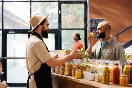 Middle Eastern male customer smells yellow fruit, that looks like a lemon, while caucasian storekeeper wearing a hat and apron looking over to the other side of counter holding a package.の写真素材