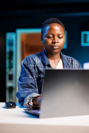 Portrait of focused african american student typing on digital laptop, working on her thesis project. Dedicated black female freelancer reviewing financial projections of company on personal computer.の写真素材