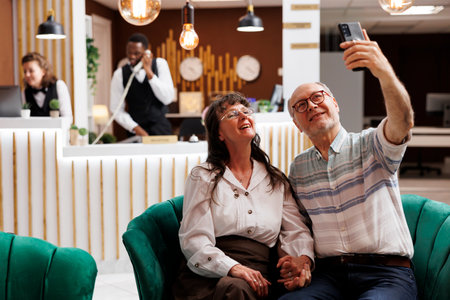 Retired caucasian couple making selfies with digital phone in luxurious hotel lobby. Excited elderly...
