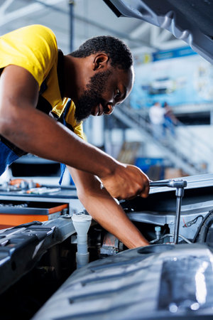Repairman in car service using professional mechanical tool to repair broken engine. Capable worker...