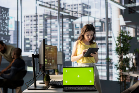 Green screen laptop in front of admin doing software quality assurance, checking source code on tablet. Chroma key notebook in office with woman at work inspecting coding on deviceの写真素材
