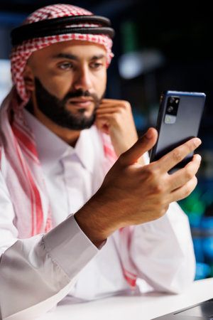 Close-up shot of Middle Eastern male adult holding his cell phone for a video conference call. Detailed view of a youthful Muslim man surfing the net on his digital mobile device.の写真素材